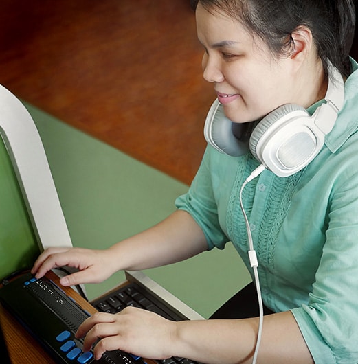 young blind woman with headphone using computer with refreshable braille display or braille terminal a technology device for persons with visual disabilities
